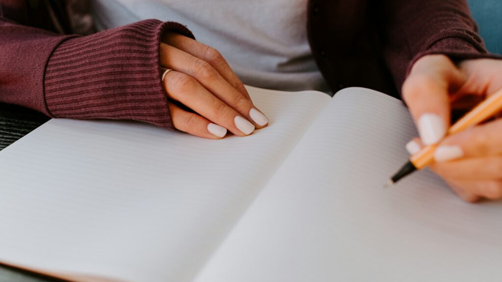 Pessoa escrevendo em um caderno para organizar seus estudos e objetivos pessoais